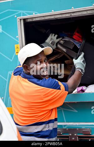 Ein Arbeiter des Gemeinderats, der den sortierten Recyclingbehälter des Haushalts mit Abfallmaterial in einen Recyclingwagen leert Stockfoto