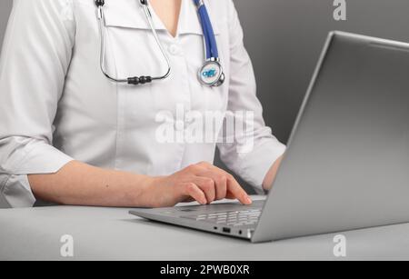 Der Arzt tippt, arbeitet am Laptop, nutzt Informationstechnologien, chattet online mit Patienten. Stockfoto