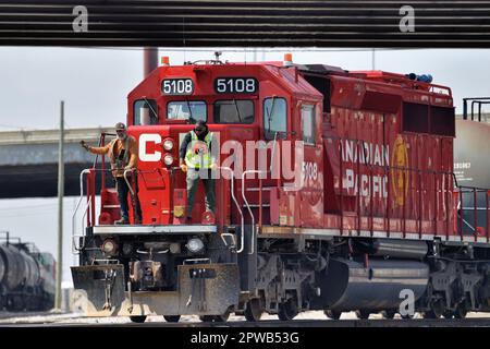 Franklin Park, Illinois, USA. Mit zwei Besatzungsmitgliedern, die auf dem vorderen Bahnsteig einer Lokomotive sitzen, wechselt ein Güterzug die Autos am Rande eines Gartens. Stockfoto