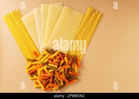 Nudeln. Verschiedene Arten roher Pasta auf beigefarbenem Hintergrund. Kreative Komposition mit Lasagne, Spaghetti und Fusilli. Italienisches Speisekonzept Stockfoto