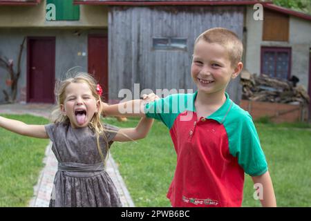 Hübsche asiatische Schulkinder, die zusammen spielen, 7 und 10 Jahre alt, mit grauem Hintergrund Stockfoto