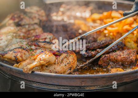 Fast-Food-Kochen. Ein Mann wirft Essen in einem großen Topf für ein Festmahl mit Zangen. Stockfoto