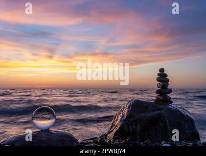 Steinpyramiden und Glaskugel am traumhaften Ostsee-Sandstrand auf Rügen für den spektakulären Sonnenuntergang Stockfoto