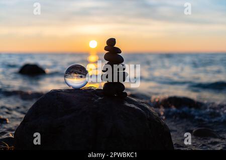 Steinpyramiden und Glaskugel am traumhaften Ostsee-Sandstrand auf Rügen für den spektakulären Sonnenuntergang Stockfoto