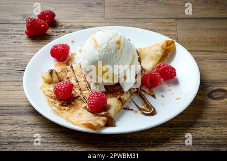 Frisch gebackene Crepes mit Eis und Himbeeren auf einem Holztisch Stockfoto