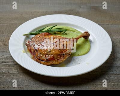 Entenschenkel-Confit und Brokkolipüree auf weißem Teller Stockfoto