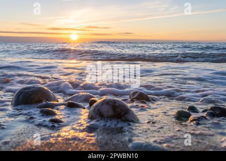 Traumhafter, orangefarbener Sonnenuntergang zwischen Felsen im Meer der Ostsee bei Dranske auf der Insel Rügen Stockfoto