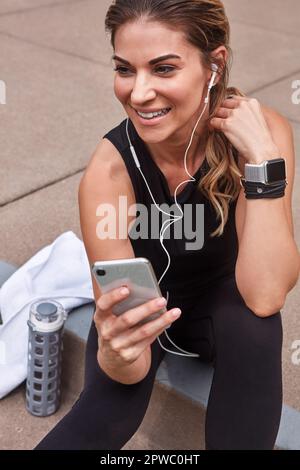 Diese Musik motiviert mich wirklich, in Bewegung zu bleiben. Eine sportliche junge Frau, die beim Sport im Freien ein Handy benutzt. Stockfoto