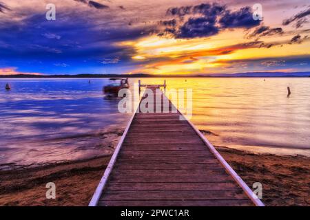 Das Fischerboot schwimmt am Holzsteg vor dem Murrays Beach Resort Beach am Lake Macquarie bei Sonnenuntergang. Stockfoto