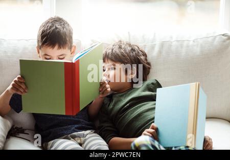 Die Familie macht die Story-Zeit noch besser. Zwei niedliche Brüder lesen Bücher, während sie sich zu Hause auf dem Sofa entspannen. Stockfoto