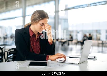 Überarbeitungskonzept. Erschöpfte frustrierte Kaukasierin, Mitarbeiter des Unternehmens, Manager, sitzt mit geschlossenen Augen am Schreibtisch, fühlt sich müde von der Arbeit, hat Stress, Migräne, hat Probleme mit der Gesundheit Stockfoto