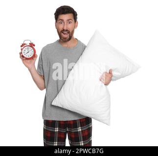 Emotional verschlafener Mann mit Wecker und Kissen auf weißem Hintergrund Stockfoto