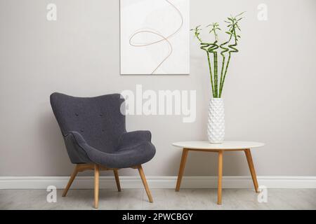 Vase mit grünen Bambusstielen und stilvollem Sessel im Zimmer. Innendesign Stockfoto