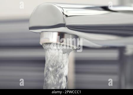 Wasser fließt aus dem Hahn auf verschwommenem Hintergrund, Nahaufnahme Stockfoto