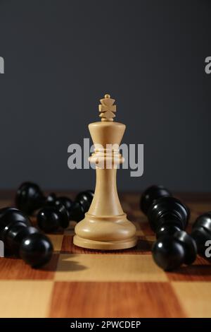 König unter gefallenen schwarzen Schachfiguren auf Holzbrett vor dunklem Hintergrund. Wettbewerbskonzept Stockfoto