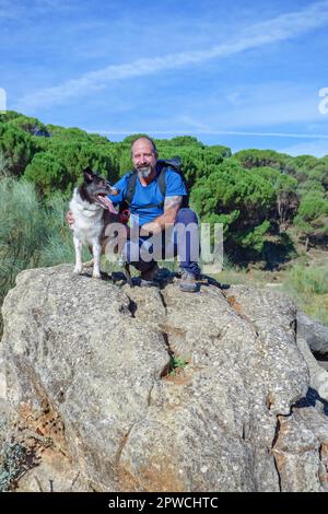 Ein Mann auf einem Felsen mit seinem Collie-Hund mit einem Kiefernwald im Hintergrund Stockfoto