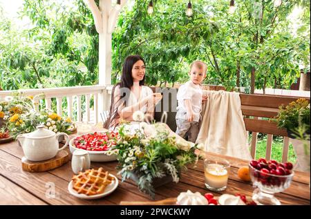 Content Frau mit niedlichen kleinen Kind in hölzernen Pavillon im Garten entspannen, während das Wochenende auf dem Land zu verbringen Stockfoto