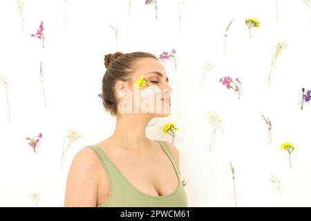 Brünett weiblich mit frischen Blumen auf ihr Gesicht mit befestigt Patches auf cremefarbenem Hintergrund am Sommertag Stockfoto