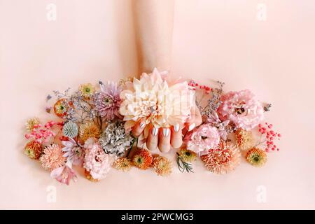 Draufsicht auf Ernte unkenntlich weiblich mit blühenden Blumen demonstrieren stilvolle gepflegte Maniküre auf rosa Hintergrund Stockfoto