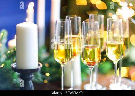 Set Champagnergläser auf Holztisch mit Kerzen gegen verwischte Wand mit Weihnachtsbaum Stockfoto