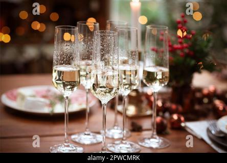 Set Champagnergläser auf Holztisch mit Kerzen gegen verwischte Wand mit Weihnachtsbaum Stockfoto