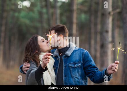 Gutaussehende Männer und Frauen in warmer Kleidung, die im Herbst die Hände mit brennenden Glitzern auf verschwommenem Hintergrund von Holz ausstreckte Stockfoto