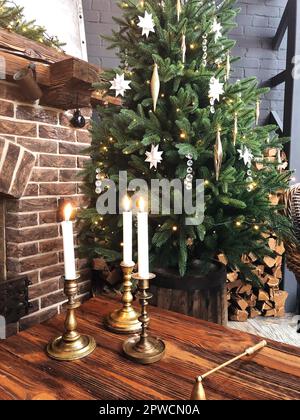 Brennende Kerzen in Vintage-Metall-Kerzenständer auf Holztisch in der Nähe für weihnachtsbaum in gemütlichen Raum mit Stein Kamin dekoriert, warme Weihnachten Stockfoto