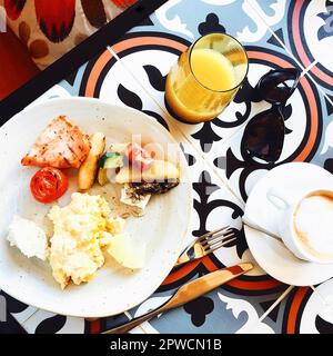 Genießen Sie ein gesundes, köstliches Frühstück im Café, Omelett mit Speck und gegrilltem Gemüse auf weißem Teller, serviert mit Orangensaft und Kaffee Stockfoto