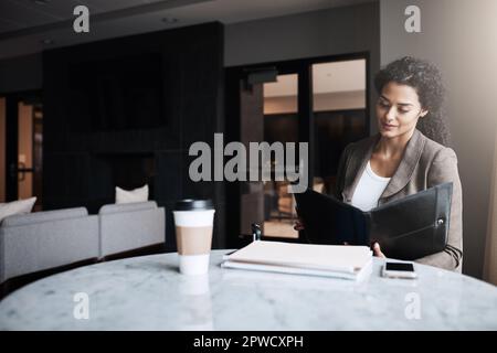 Sie ist immer gut vorbereitet im Geschäft. Eine junge Geschäftsfrau, die in einem Café eine Geschäftsmappe liest. Stockfoto