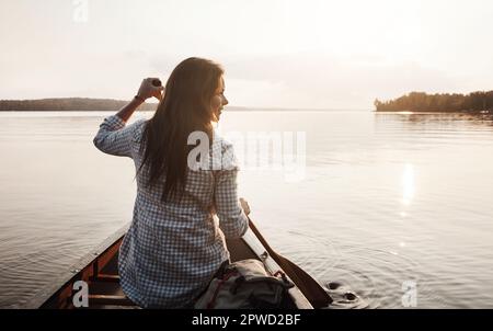 Paddeln zu neuen Abenteuern. Rückansicht einer jungen Frau, die eine Kanufahrt auf dem See genießt. Stockfoto