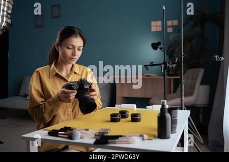 Hispanische Fotografin, die Kosmetikprodukte auf dem Tisch im Heimstudio schießt. Professionelle Fotografie. Stockfoto