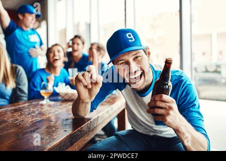 Als erster Platz nach Hause. Porträt eines Mannes, der einen Finger hochhält, während er sich ein Sportspiel mit Freunden in einer Bar ansieht. Stockfoto