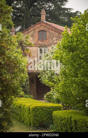 Landhaus aus Stein mit Terrakottafliesen, umgeben von einem Garten im italienischen Stil mit Bäumen und Hecken im Schloss San Sebastiano da Po, Italien Stockfoto