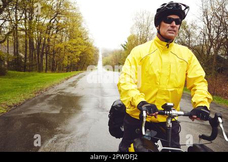 Lassen Sie sich vom Wetter nicht aufhalten. Ein männlicher Radfahrer genießt eine Fahrradtour an einem nassen Wintermorgen. Stockfoto