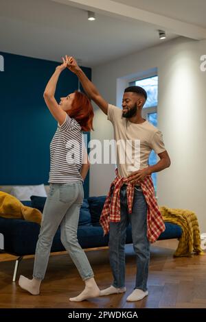 Liebevolles junges, vielfältiges Paar, das romantischen Tanz im modernen Schlafzimmer mit Panoramafenstern tanzt. Stockfoto