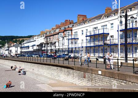 Blick auf die Hotels entlang der Promenade vom Strand aus mit Touristen, die die Umgebung genießen, Sidmouth, Devon, Großbritannien. Stockfoto