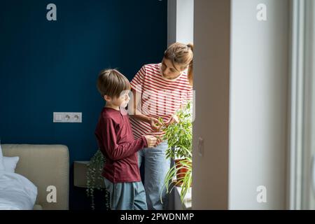 Junge Mutter, die ihrem Sohn beibringt, wie man sich um Zimmerpflanzen kümmert Stockfoto