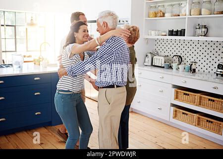 Diese Familie hat keine Angst, ihre Liebe zu zeigen. Eine liebevolle Familie, die sich in der Küche zu Hause mit Umarmungen begrüßt. Stockfoto