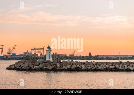 Sonnenuntergangslandschaft mit dem Genuesischen Leuchtturm mit blauem Dach, vom Pier aus aus Felsen, in einem Hafen am Schwarzen Meer. Stockfoto