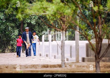 (230430) -- YECHENG, 30. April 2023 (Xinhua) -- Dieses am 30. April 2011 aufgenommene Aktenfoto zeigt Emer Yit, zusammen mit seinen Enkeln, die die Gräber auf dem Yecheng-Märtyrerfriedhof in Yecheng, Nordwestchina Autonomer Region Xinjiang Uygur, fegen. Jeden April blühen Blumen auf dem Friedhof der Yecheng-Märtyrer in der Autonomen Region Xinjiang Uygur im Nordwesten Chinas, wo 233 Märtyrer begraben wurden. „Ich werde mich gut um den Friedhof kümmern“, sagte der 53-jährige Eniwar Emer vor dem Grabstein seines Vaters. Eniwar ist ein Hüter der zweiten Generation auf dem Friedhof der Yecheng-Märtyrer, der den Spuren folgt Stockfoto