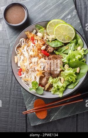 Vietnamesischer Rindernudelsalat Pho Tron Nahaufnahme auf dem Teller auf dem Holztisch. Vertikale Draufsicht von oben Stockfoto