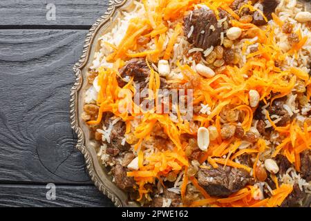 Afghanisches Nationalgericht Kabuli Pulao Reispilaf mit Lamm und Rosinen, Karotten, Nüssen, Gewürzen, die auf dem Holztisch auf dem Teller aufliegen. Horizontale Draufsicht f Stockfoto