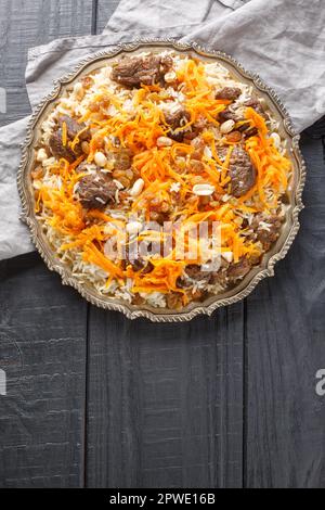 Köstlicher bunter afghanischer Reispilaf Kabuli pulao mit Lamm und Rosinen, Karotten, Nüssen und Gewürzen, die auf dem Holztisch auf dem Teller verstaut werden. Vertikale Draufsicht Stockfoto