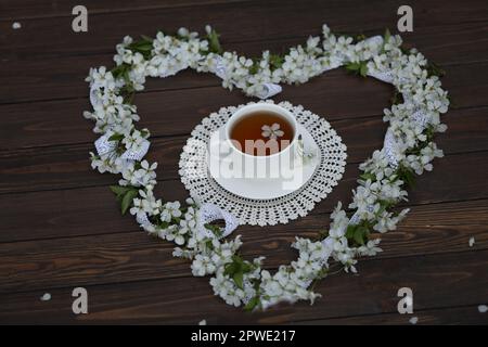 tasse Tee mit Kirschblüten, herzförmige Dekoration auf dunkelbraunem Holzhintergrund Stockfoto