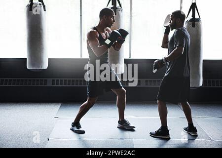 Er hat das Potenzial, etwas großartiges zu sein. Ein männlicher Boxer, der seine Bewegungen mit seinem Trainer übt. Stockfoto