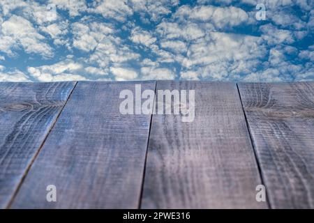 Leerer Holztisch und wunderschöner blauer Himmel und weiße Wolken im Hintergrund. Perspektivische braune Holzbretter Stockfoto
