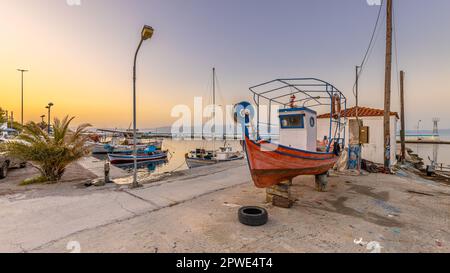 Fischerhafen Szene in Griechenland mit Booten, Palmen und Motorroller bei Sonnenaufgang auf einem schönen, ruhigen Sommer Tag Stockfoto