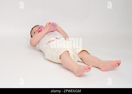 Happy Baby trinkt Milch aus der Flasche auf weißem Studiohintergrund. Ruhendes Kind isst Formel. Kind etwa zwei Jahre alt (ein Jahr neun Monate) Stockfoto