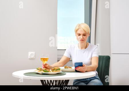 Seniorin liest Morgennachrichten vom Smartphone, während sie frühstückt Stockfoto