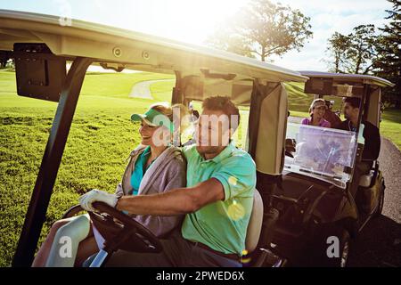 Mit anderen Paaren auf dem Platz. Eine Gruppe von Freunden, die in einem Golfwagen auf einem Golfplatz reiten. Stockfoto